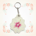 Cream and pink hibiscus keychain on a pale tropical background without a shadow